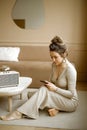 a young caucasian woman in a stylish apartment looking at her phone, a fashionable lady sitting on the floor writing Royalty Free Stock Photo