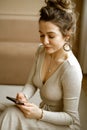 a young caucasian woman in a stylish apartment looking at her phone, a fashionable lady sitting on the floor writing Royalty Free Stock Photo