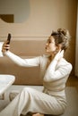 a young caucasian woman in a stylish apartment looking at her phone, a fashionable lady sitting on the floor writing Royalty Free Stock Photo