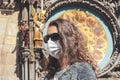 Young Caucasian woman with sunglasses and medical face mask photographed in front of the Astronomical clock Orloj in Prague, Czech