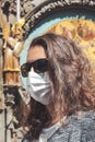 Young Caucasian woman with sunglasses and medical face mask photographed in front of the Astronomical clock Orloj in Prague, Czech