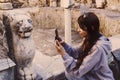 Young caucasian woman taking photo of ancient stone sculpture of panter. Selective focus