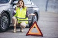 Young woman, talking on her cell phone while her car is broken down on the road with reflective warning triangles Royalty Free Stock Photo
