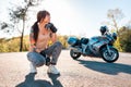 Young caucasian woman with tattoos on her arm, wearing motorcycle gloves posing sitting. Road and motorbike in the