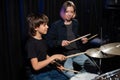 Young caucasian woman teaches a boy to play the drums in the studio on a black background. Music school student