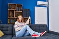 Young caucasian woman using air condition machine sitting on sofa at home Royalty Free Stock Photo