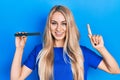 Young caucasian woman using file nail smiling with an idea or question pointing finger with happy face, number one