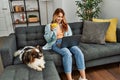 Young caucasian woman using laptop drinking coffee sitting on sofa with dog at home Royalty Free Stock Photo