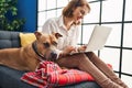 Young caucasian woman using laptop sitting on sofa with dog at home Royalty Free Stock Photo