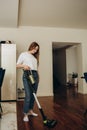 A young Caucasian woman vacuums a kitchen floor using a cordless vertical vacuum cleaner, or electric broom. The maid is Royalty Free Stock Photo