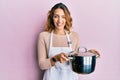 Young caucasian woman wearing apron holding cooking pot winking looking at the camera with sexy expression, cheerful and happy Royalty Free Stock Photo