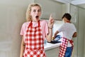 Young caucasian woman wearing apron and husband doing housework washing dishes pointing finger up with successful idea Royalty Free Stock Photo