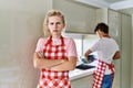 Young caucasian woman wearing apron and husband doing housework washing dishes skeptic and nervous, disapproving expression on Royalty Free Stock Photo