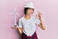 Young caucasian woman wearing architect hardhat holding windmill doing ok sign with fingers, smiling friendly gesturing excellent Royalty Free Stock Photo