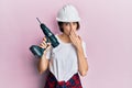 Young caucasian woman wearing architect hardhat using drill covering mouth with hand, shocked and afraid for mistake Royalty Free Stock Photo