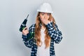 Young caucasian woman wearing architect hardhat using drill covering mouth with hand, shocked and afraid for mistake Royalty Free Stock Photo