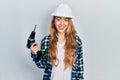 Young caucasian woman wearing architect hardhat using drill looking positive and happy standing and smiling with a confident smile Royalty Free Stock Photo