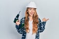 Young caucasian woman wearing architect hardhat using drill pointing thumb up to the side smiling happy with open mouth Royalty Free Stock Photo