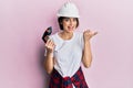Young caucasian woman wearing architect hardhat using drill pointing thumb up to the side smiling happy with open mouth Royalty Free Stock Photo