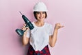 Young caucasian woman wearing architect hardhat using drill pointing thumb up to the side smiling happy with open mouth Royalty Free Stock Photo