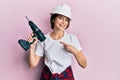 Young caucasian woman wearing architect hardhat using drill smiling happy pointing with hand and finger Royalty Free Stock Photo