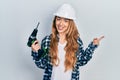 Young caucasian woman wearing architect hardhat using drill smiling happy pointing with hand and finger to the side Royalty Free Stock Photo