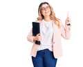 Young caucasian woman wearing business clothes and glasses holding binder surprised with an idea or question pointing finger with Royalty Free Stock Photo