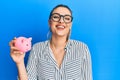 Young caucasian woman wearing business clothes holding piggy bank looking positive and happy standing and smiling with a confident Royalty Free Stock Photo