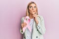 Young caucasian woman wearing business clothes holding pink cancer ribbon serious face thinking about question with hand on chin, Royalty Free Stock Photo