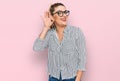 Young caucasian woman wearing business shirt and glasses smiling with hand over ear listening an hearing to rumor or gossip Royalty Free Stock Photo