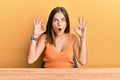 Young caucasian woman wearing casual clothes sitting on the table looking surprised and shocked doing ok approval symbol with Royalty Free Stock Photo