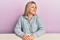 Young caucasian woman wearing casual clothes sitting on the table looking to side, relax profile pose with natural face and Royalty Free Stock Photo