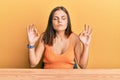 Young caucasian woman wearing casual clothes sitting on the table relaxed and smiling with eyes closed doing meditation gesture Royalty Free Stock Photo