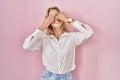 Young caucasian woman wearing casual white shirt over pink background covering eyes with hands smiling cheerful and funny Royalty Free Stock Photo