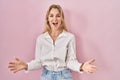 Young caucasian woman wearing casual white shirt over pink background smiling cheerful with open arms as friendly welcome, Royalty Free Stock Photo