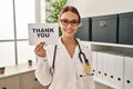 Young caucasian woman wearing doctor uniform holding thank you banner looking positive and happy standing and smiling with a Royalty Free Stock Photo