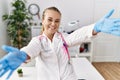 Young caucasian woman wearing doctor uniform and stethoscope at the clinic looking at the camera smiling with open arms for hug Royalty Free Stock Photo