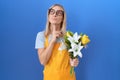 Young caucasian woman wearing florist apron holding flowers thinking concentrated about doubt with finger on chin and looking up