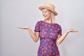 Young caucasian woman wearing flowers dress and summer hat smiling showing both hands open palms, presenting and advertising Royalty Free Stock Photo