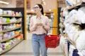 Young Caucasian woman wearing glasses holds grocery basket, holds list and selects bed linen. Shopping concept