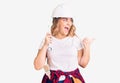 Young caucasian woman wearing hardhat holding wrench pointing thumb up to the side smiling happy with open mouth Royalty Free Stock Photo