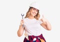 Young caucasian woman wearing hardhat holding wrench smiling happy and positive, thumb up doing excellent and approval sign Royalty Free Stock Photo