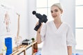 Young caucasian woman wearing physio therapist uniform using percussion pistol at clinic