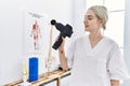 Young caucasian woman wearing physio therapist uniform using percussion pistol at clinic