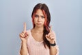 Young caucasian woman wearing pink sweater over isolated background pointing up looking sad and upset, indicating direction with