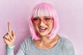 Young caucasian woman wearing pink wig and heart sunglasses smiling happy pointing with hand and finger to the side Royalty Free Stock Photo