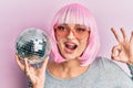 Young caucasian woman wearing pink wig holding disco ball doing ok sign with fingers, smiling friendly gesturing excellent symbol Royalty Free Stock Photo