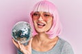 Young caucasian woman wearing pink wig holding disco ball looking positive and happy standing and smiling with a confident smile Royalty Free Stock Photo