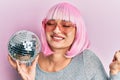 Young caucasian woman wearing pink wig holding disco ball screaming proud, celebrating victory and success very excited with Royalty Free Stock Photo