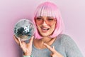 Young caucasian woman wearing pink wig holding disco ball smiling happy pointing with hand and finger Royalty Free Stock Photo